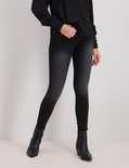Model in zwarte skinny jeans en zwarte laarsjes.