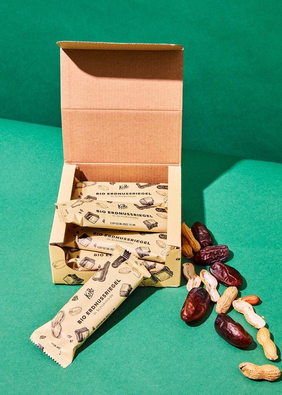 Een open bruine doos met 4 repen biologische pindarepen met chocolade. Er liggen ook dadels en pinda's naast.
