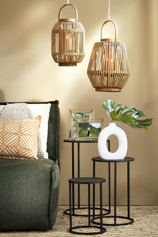 Twee rotan hanglampen met een cilindrische vorm, boven een groene bank met decoratieve kussens.