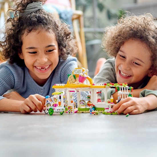 Twee lachende kinderen kijken naar een LEGO Friends café set met een smoothiekar.