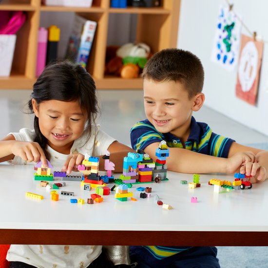 Twee kinderen die aan een tafel spelen met LEGO Classic blokjes en hun creaties.