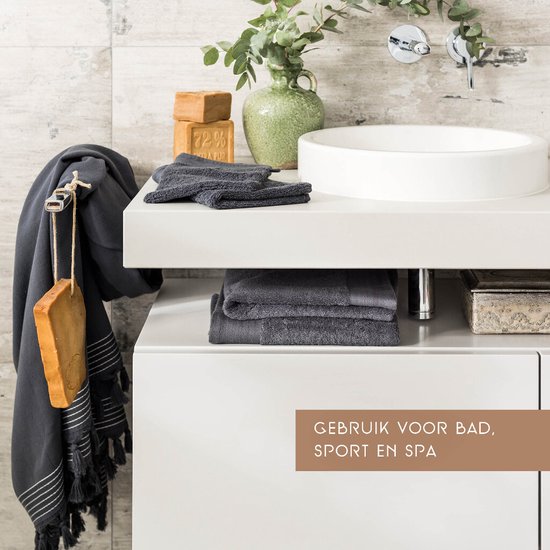 Badkamerinterieur met een antracietkleurige handdoek met franjes aan een haak, zeepblokken en een kraan.