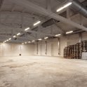Grote, lege opslagruimte met hoge plafonds, betonnen vloer en tl-verlichting.
