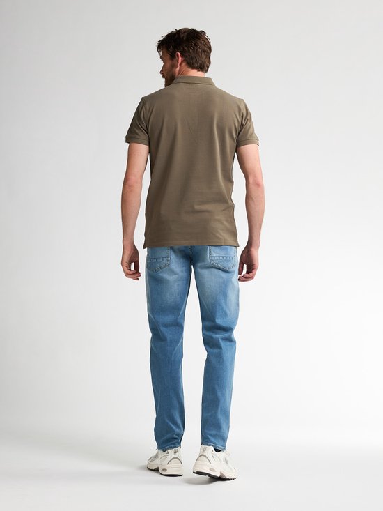 Achterkant van een man in een olijfgroen poloshirt en blauwe jeans, staand tegen een witte achtergrond.