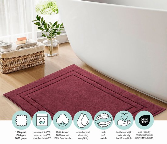Bordeauxrode badmat naast een bad. Iconen tonen 1000 g/m², wassen tot 60°C, 100% katoen, absorberend, zacht, huidvriendelijk en oekotex.