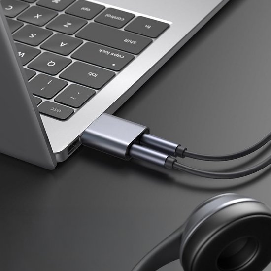 Grijze QOST USB geluidskaart adapter aangesloten op een laptop met hoofdtelefoon.