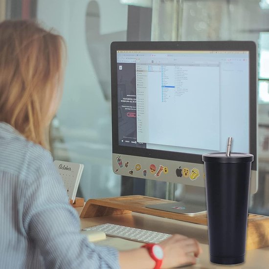 Zwarte thermobeker met rietje op een bureau naast een computer en toetsenbord, op kantoor.