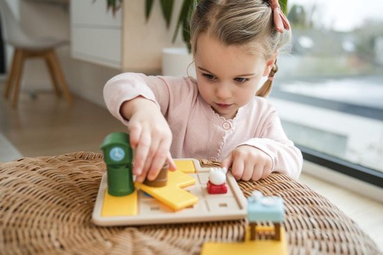 Une jeune fille avec un ruban rouge dans les cheveux joue avec le jeu 'Le Loup et les 7 Chevreaux Deluxe'.