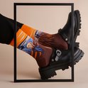 Model draagt zwarte broek, zwarte klomp-sneakers en sokken met Munchs Schreeuw in oranje en bruin.