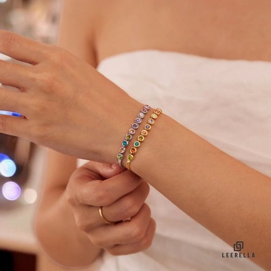 Hand van een vrouw draagt een zilverkleurige en een goudkleurige armband met veelkleurige stenen.