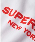 Femme portant un sweat Superdry blanc avec l'inscription rouge "SUPERDRY NEW YORK".