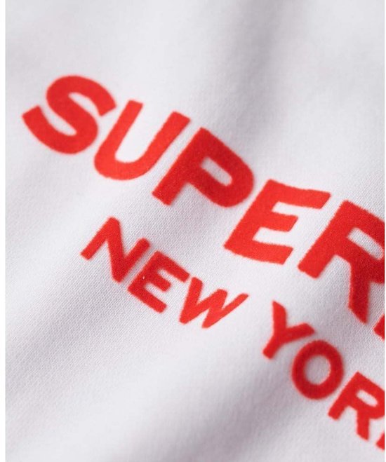 Femme portant un sweat Superdry blanc avec l'inscription rouge "SUPERDRY NEW YORK".