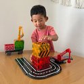 Jongetje speelt met Magna-Tiles. Een hijskraan met een groene lading staat naast een stapel rode en gele blokken op een speelgoedweg.