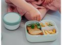 Main d'enfant prenant une mini-fourchette dans une boîte bento vert pâle avec un sandwich et de la salade.