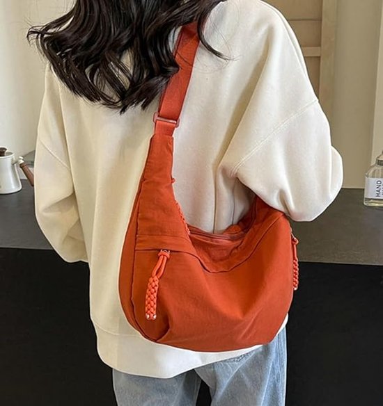 Vrouw met oranje dumpling tas over de schouder, gedragen over een witte trui en spijkerbroek.