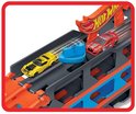 Grijze Hot Wheels trailer met oranje en blauwe accenten, met gele en rode raceauto's die vanaf de baan lanceren.