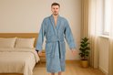 Homme dans une chambre, portant une robe de chambre bleu clair, douce, avec ceinture et poches plaquées.