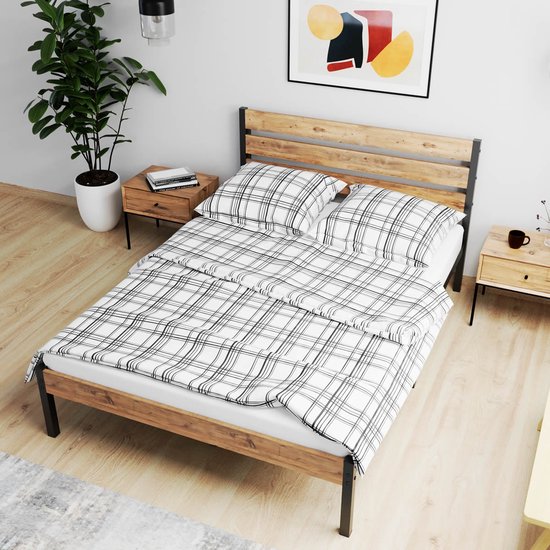 Bedframe met houten hoofdbord, zwart metalen frame en een wit/zwart geruite deken en kussens.