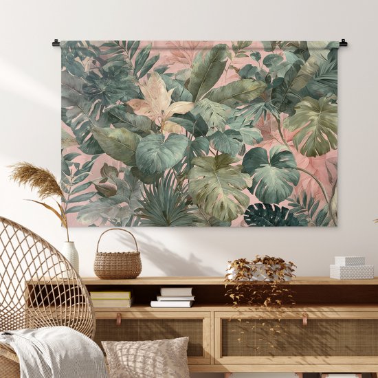 Een tropische bladerenprint in groen en roze op een wandkleed, hangend boven een houten dressoir met een stoel.