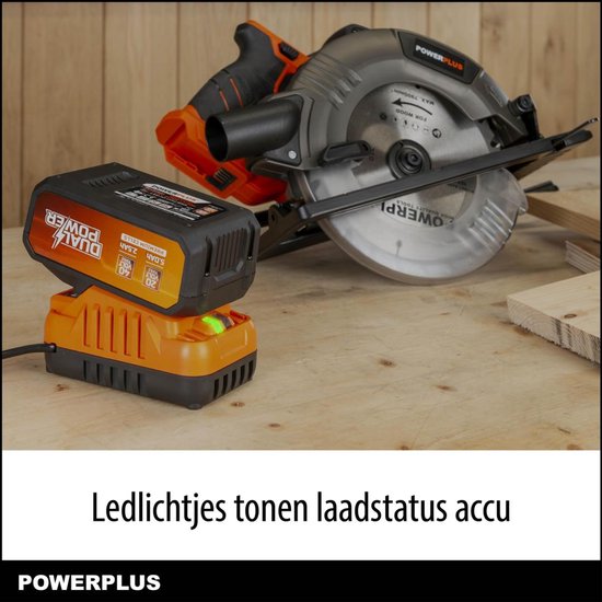Oranje Dual Power accu op oranje lader met groene LED, met een cirkelzaag op de achtergrond.