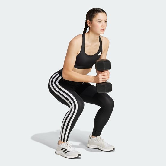 Model in zwarte legging met witte Adidas strepen maakt een squat met een dumbbell