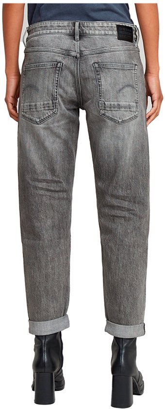 Model draagt een grijze jeans met opgerolde broekspijpen en zwarte laarzen.