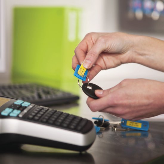 Handen bevestigen een geel label aan een blauw sleutelhangertje met een Dymo labelmaker op de voorgrond.