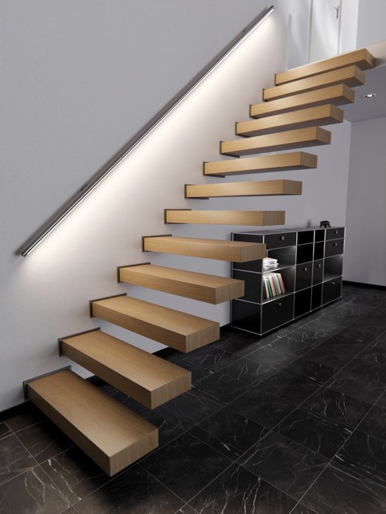 Marches d'escalier flottantes en bois éclairées par une bande lumineuse le long du mur, avec une armoire noire en bas.