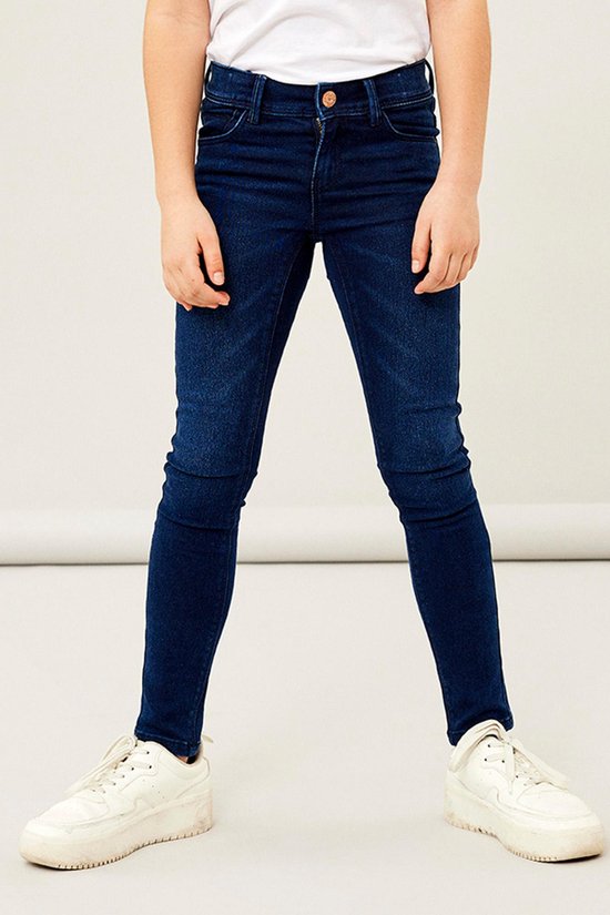 Een meisje in een donkerblauwe skinny jeans met witte sneakers.