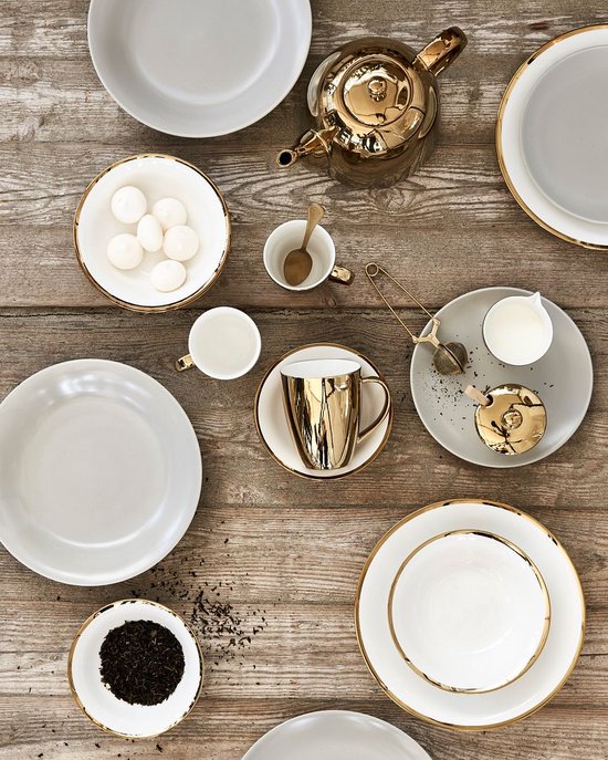 Onderdeel van een gedekte tafel met witte en gouden kommen, borden en kopjes.