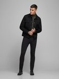 Model draagt een zwarte spijkerjack, een groene coltrui en zwarte skinny jeans.