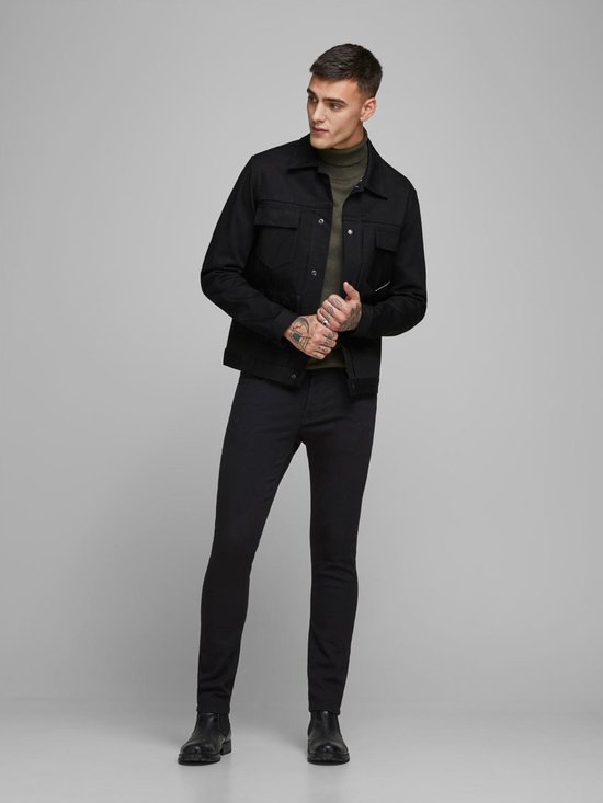 Model draagt een zwarte spijkerjack, een groene coltrui en zwarte skinny jeans.