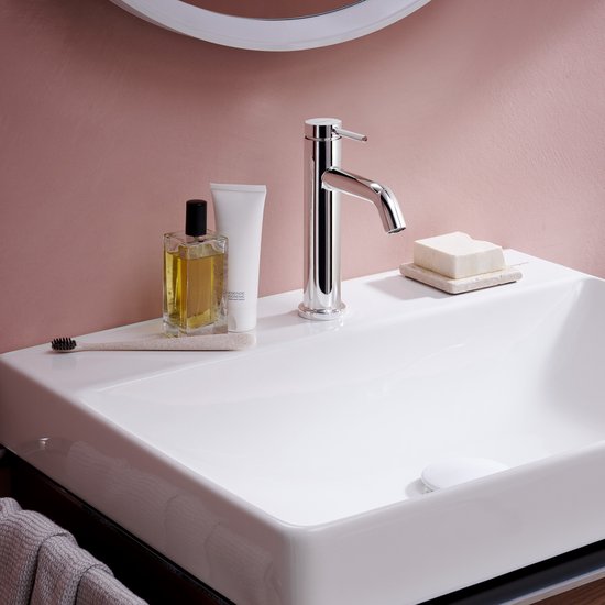 Chromen wastafelkraan naast toiletartikelen op een witte wastafel.