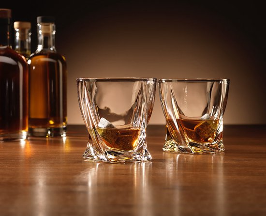 Deux verres torsadés remplis avec des pierres sur une table en bois, avec des bouteilles en arrière-plan.