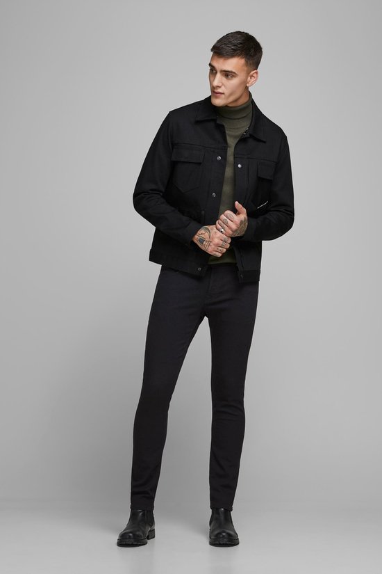 Man in een zwarte spijkerjas en zwarte skinny jeans.