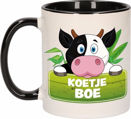 Wit met zwart handvat mok met een cartoon koe met de tekst 'KOETJE BOE' op een groen houten bord.