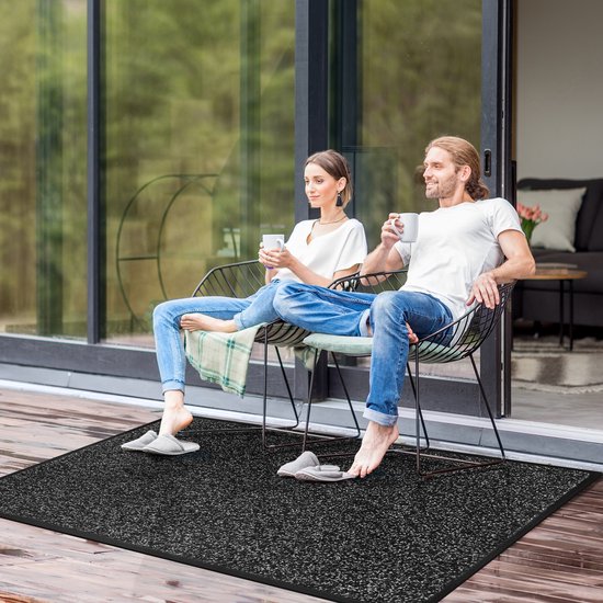 Koppel zit buiten op stoelen, met mokken, op een grijze, gemêleerde deurmat.