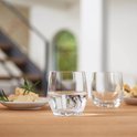 Twee glazen water met bubbels op een houten tafel, met kaas en brood op de achtergrond.