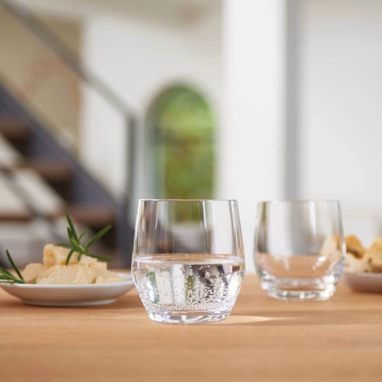 Twee glazen water met bubbels op een houten tafel, met kaas en brood op de achtergrond.