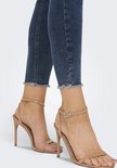 Close-up van de enkels van een model in beige sandalen en donkerblauwe skinny jeans met rafels.