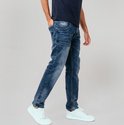 Blauwe spijkerbroek met stone wash, gedragen door een man met witte sneakers en een donkerblauw T-shirt.
