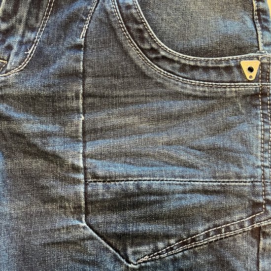 Detail van een blauwe jeans met stone wash used look en opvallende naden.