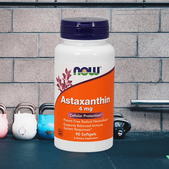 NOW Astaxanthin 4 mg, 90 softgels, in een fles met paars deksel, voor een bakstenen muur met gewichten.
