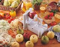 Een witte spiraalsnijder snijdt een rode appel in dunne slierten, omringd door verse groenten en fruit.