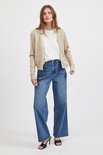 Model met lange haren draagt een beige gebreid vest met witte top en wijde jeans.