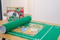 Groene puzzelmat opgerold met een gedeeltelijk gelegde puzzel. Naast de doos met illustraties.