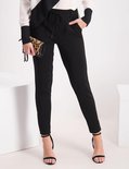 Model draagt zwarte broek met ceintuur en hoge hakken, met een dierenprint clutch.