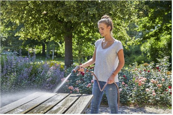Vrouw sproeit een houten picknicktafel in een tuin met een Gardena spuitpistool.