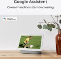 Een tablet met het Google Assistant logo toont een videostream van een kind dat speelt. Een vaas met eucalyptus staat ernaast.