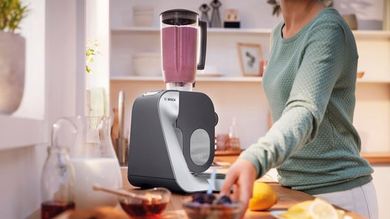 Robot de cuisine gris foncé avec blender, une femme prépare un smoothie.